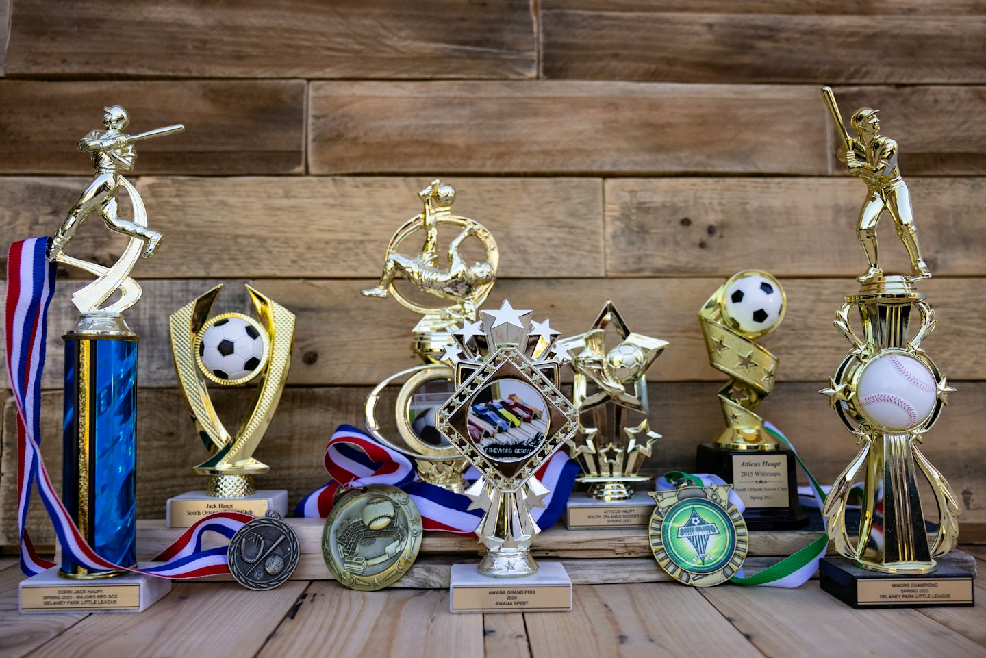 Coppe sportive e medaglie esposte su un tavolo di legno rustico.