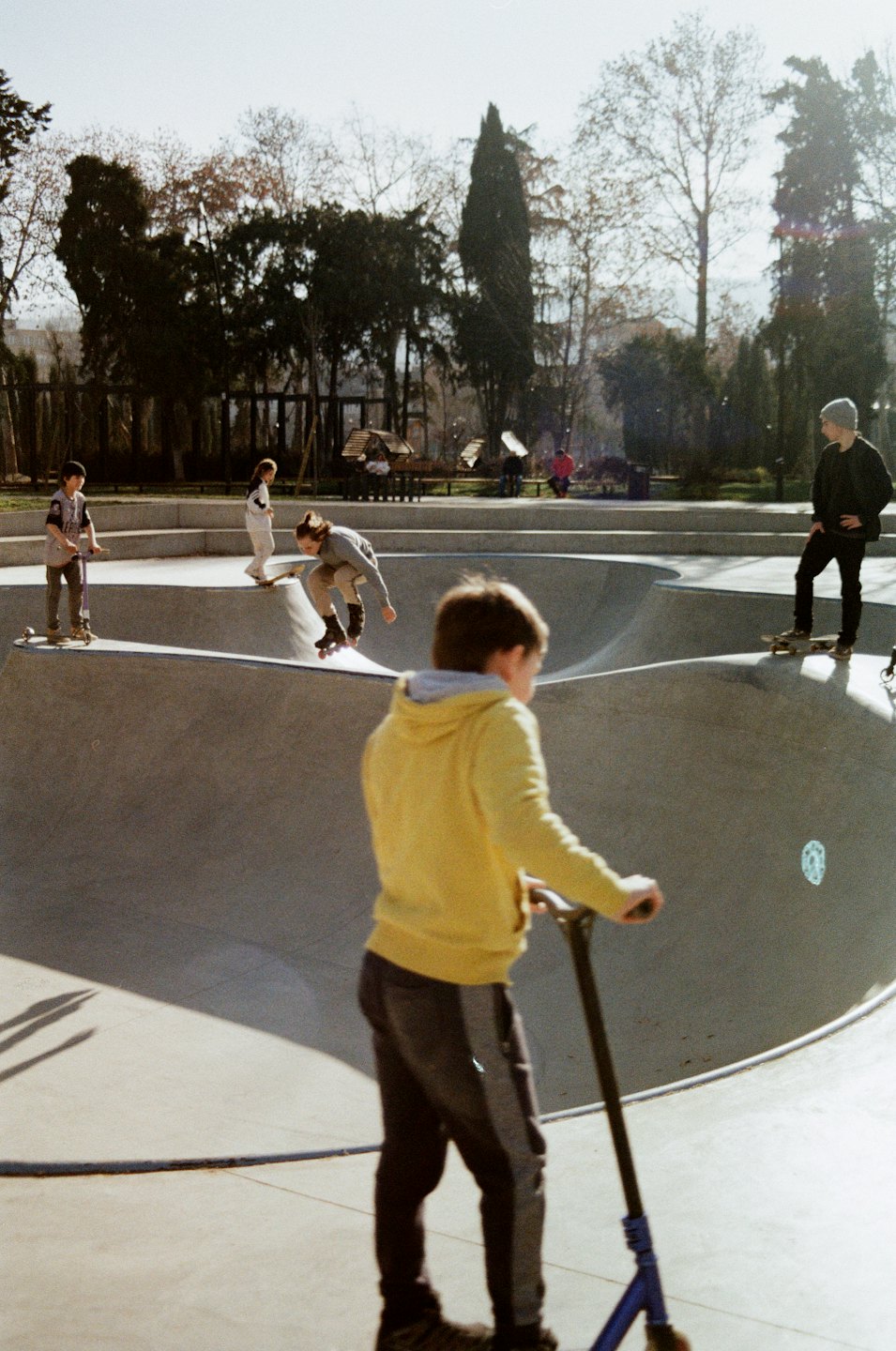 Persone in monopattino e skateboard in un parco di cemento all'aperto.