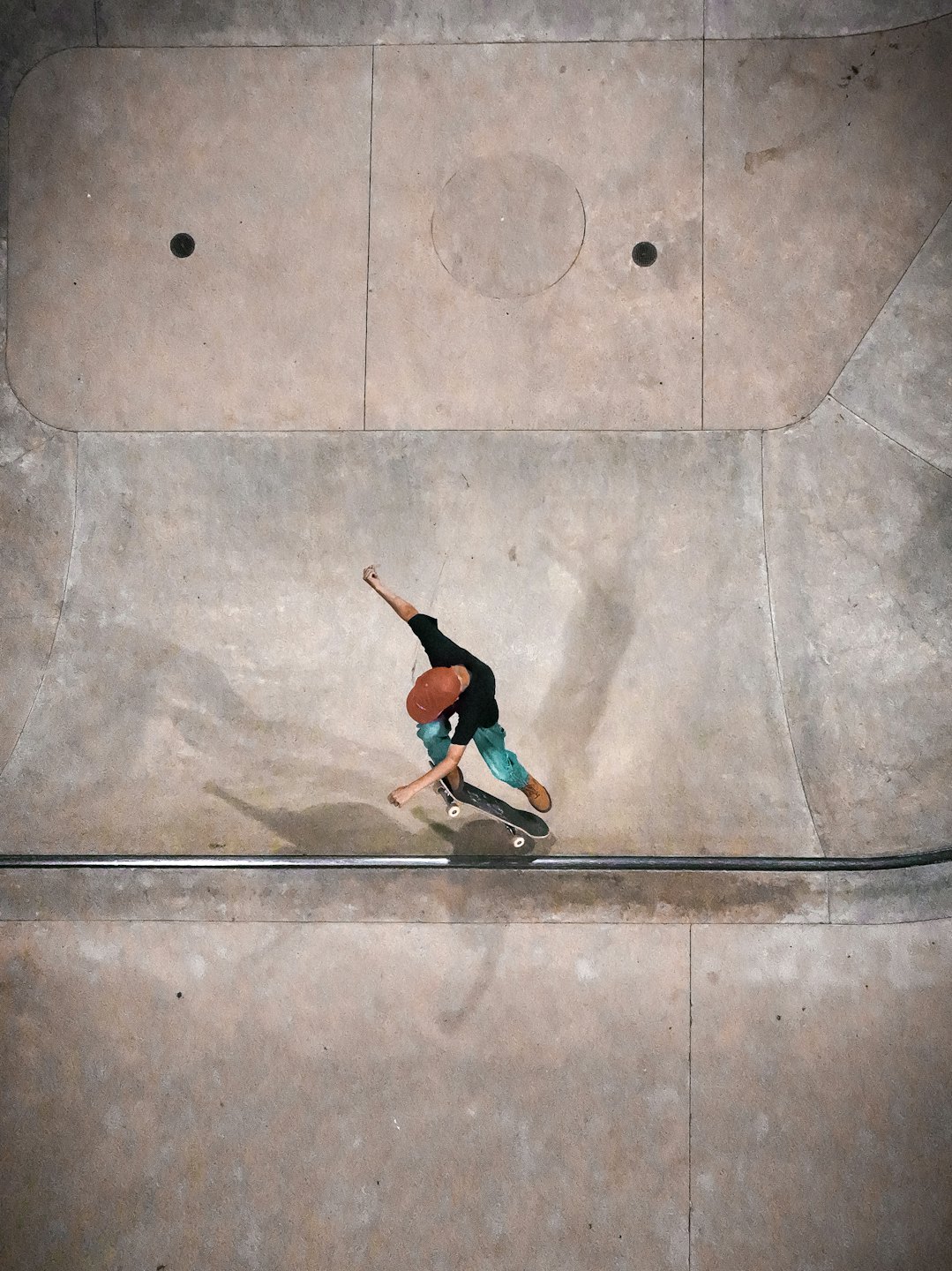 Skater in pantaloni color acqua fa una curva in uno skatepark di cemento.
